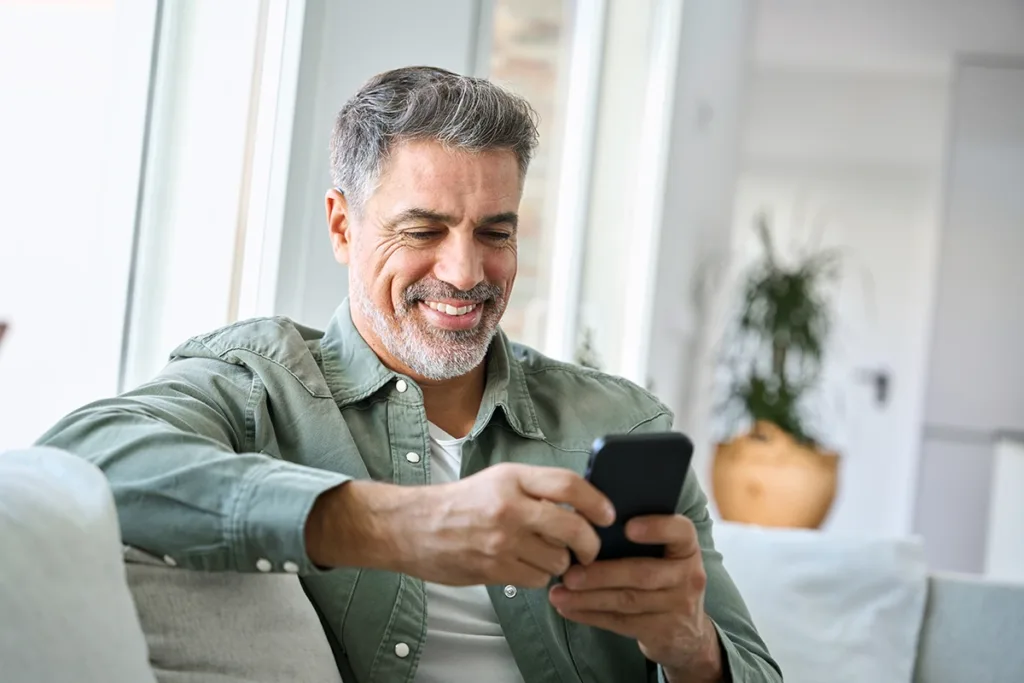 A middle aged man wearing an AI hearing aid and happily using an AI hearing aid app